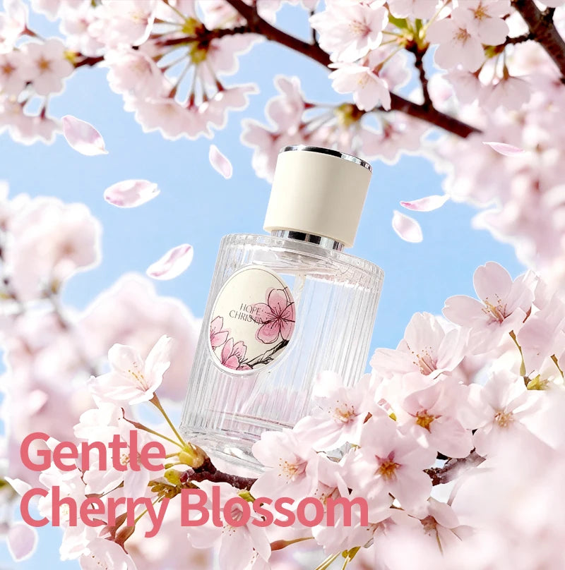 Glass perfume bottle with cream cap, floral Sakura label, surrounded by pink cherry blossoms against a blue sky.