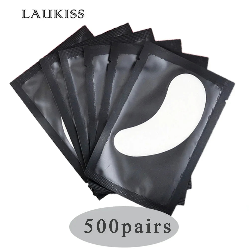 White gel eyelash extension under eye patches in individual black wrappers for professional lash application.