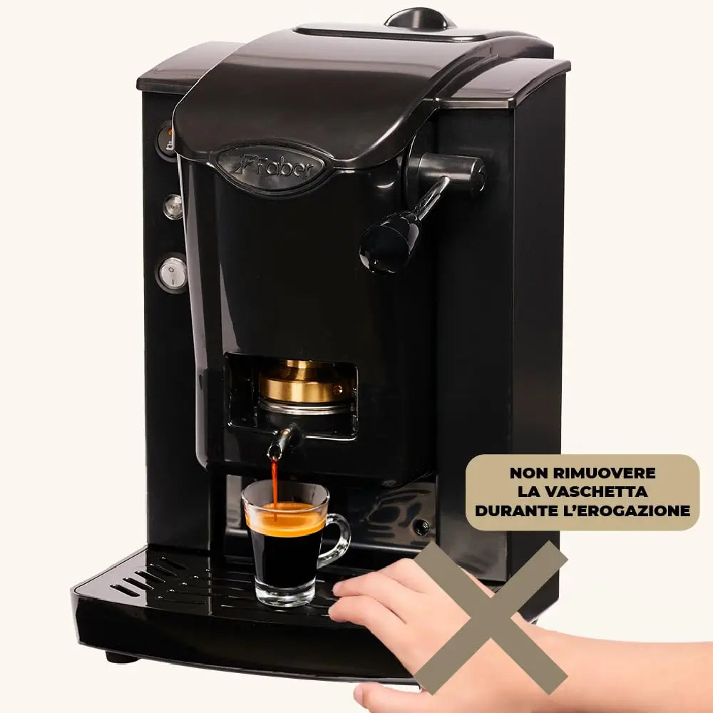 Faber black pod espresso machine brewing coffee into a glass cup with caution sign against removing water tray.
