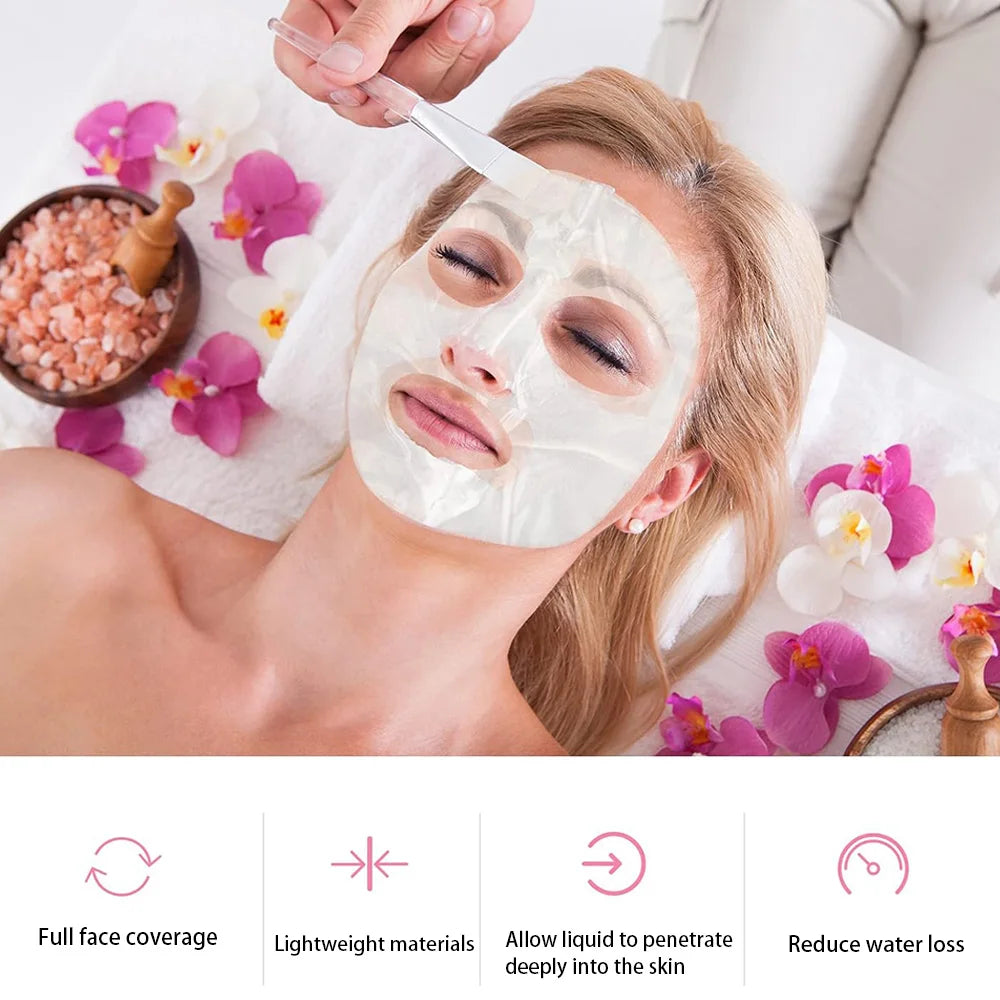 A woman with a thin, transparent DIY facial mask on, as a beautician applies product with a brush in a spa setting.