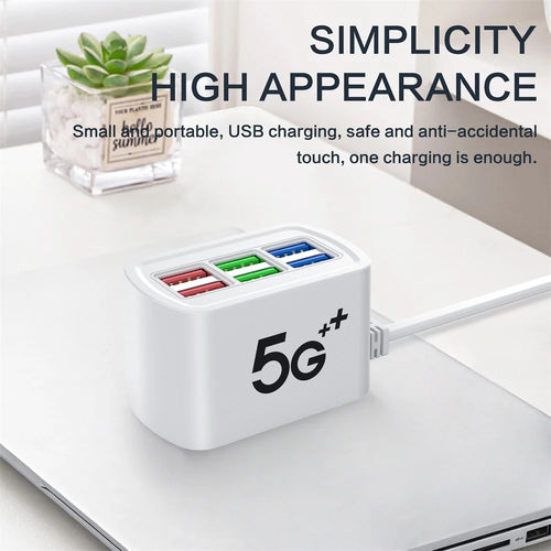 White 6-port USB charging station with four colored ports on a desk beside a wall plug