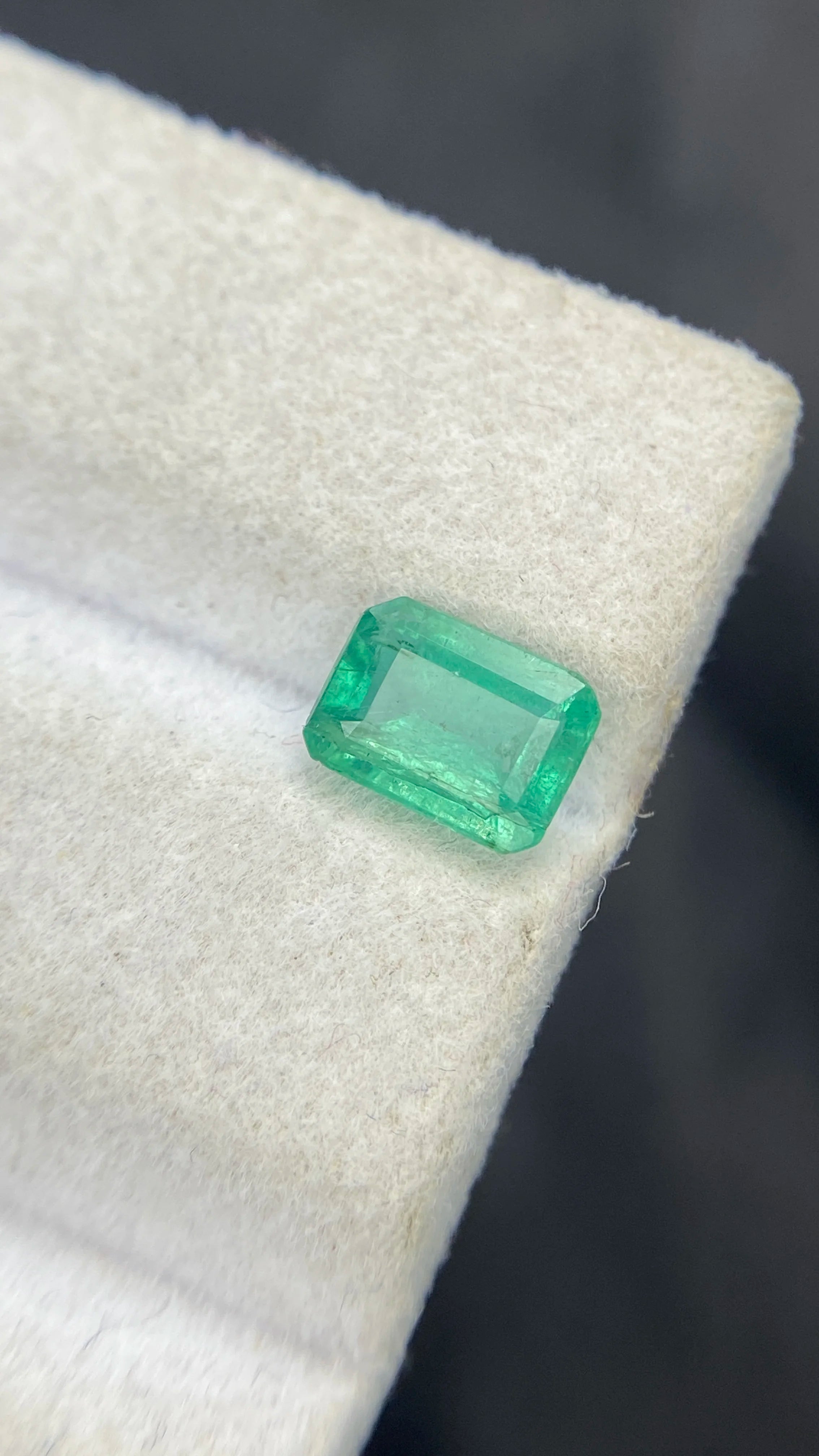 Loose emerald-cut green gemstone, tilted close-up on white felt pad