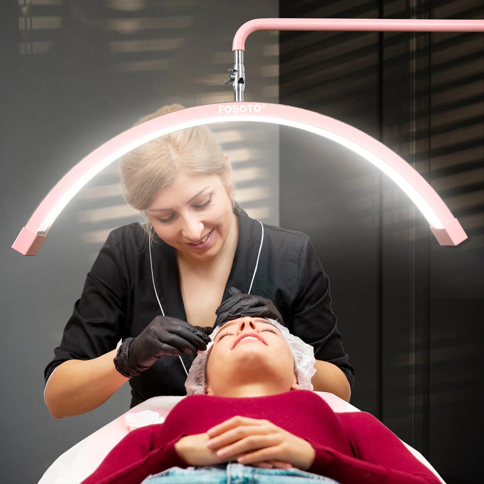 Pink arched LED beauty lamp positioned over a client receiving a facial treatment.