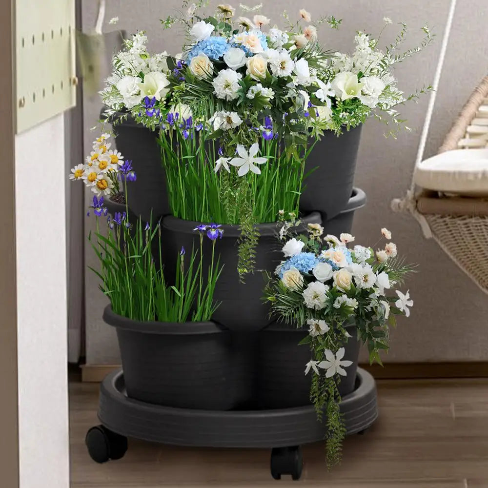 Three stacked dark gray planter pots filled with flowers on a wheeled tower