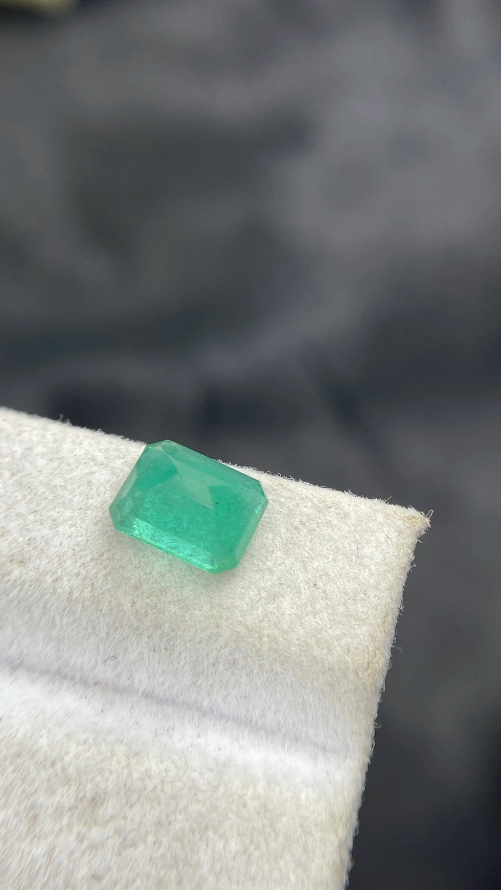 Angled view of emerald-cut green gemstone on white felt