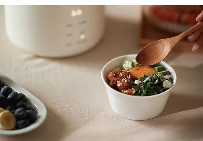 White ceramic inner pot with cooked food, served with spoon from electric cooker