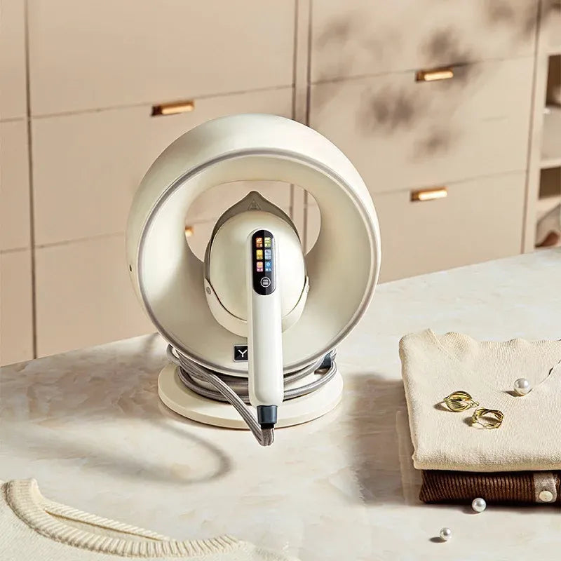 Handheld garment steamer with digital display docked in a modern cream ring base on a marble table with folded sweaters.