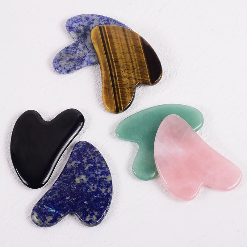 Five heart-shaped gua sha massage tools made from various polished stones including rose quartz, jade, and lapis lazuli.