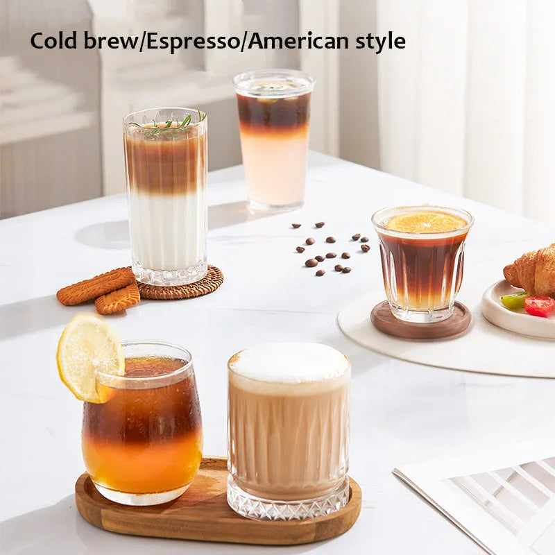 Clear textured glass coffee cups for cold brew, espresso, and iced lattes on wooden coasters.