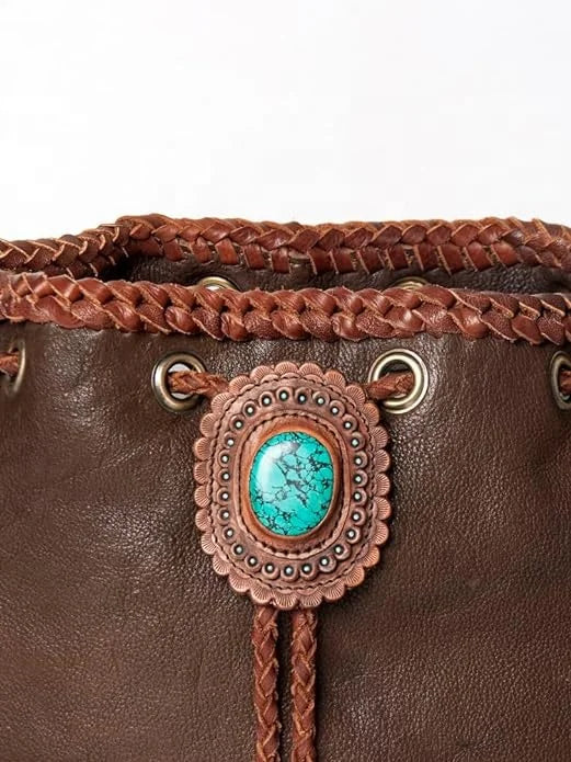 Brown leather bucket bag with braided trim, turquoise stone concho accent, and drawstring closure. Western trunk style.