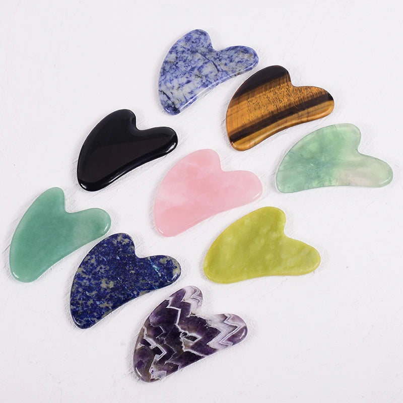 A collection of nine heart-shaped gua sha facial massage tools in various colors and natural stone textures.