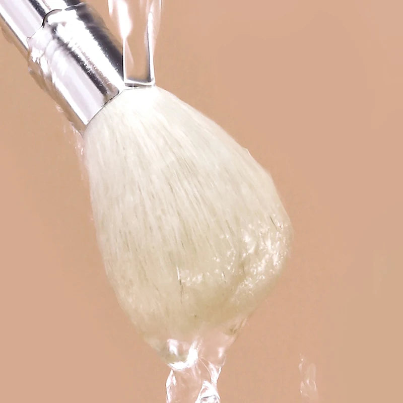 Soft white facial cleanser and mask brush rinsing under a stream of water for skincare and face massage.