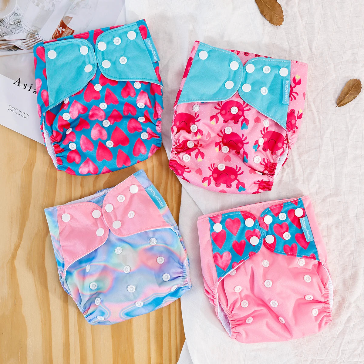 Four Happy Flute reusable cloth baby diapers featuring colorful heart, crab, and iridescent patterns with snap closures.