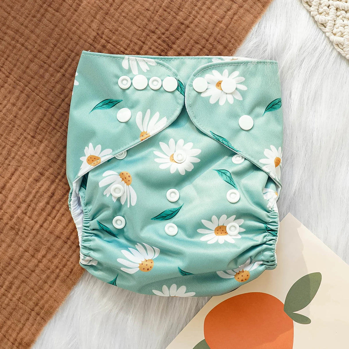 Reusable cloth baby diaper with adjustable snaps and cute white daisy print on mint green background.