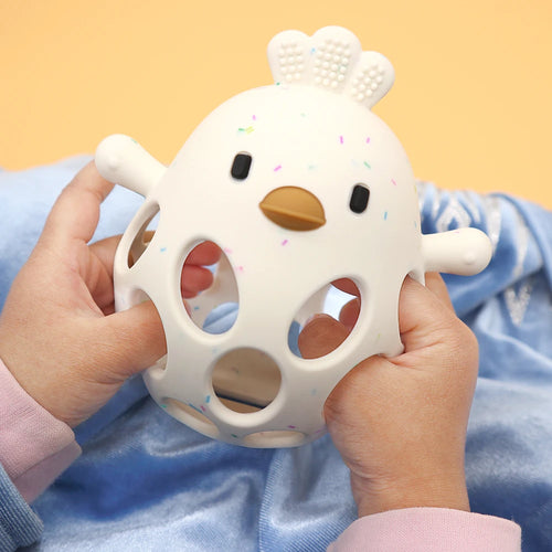 White silicone baby teething toy with colorful confetti spots held by a baby's hands.