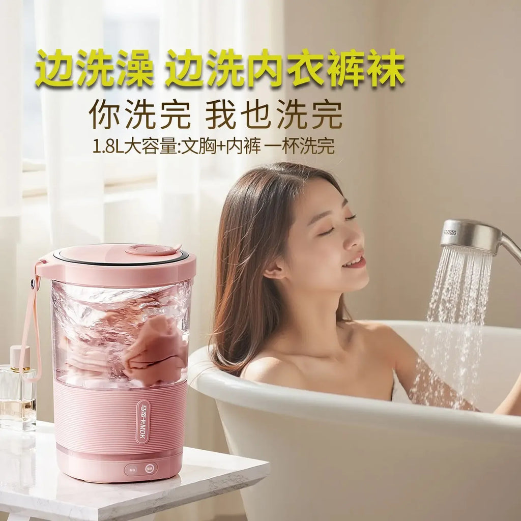 Mini washing machine washing clothes in a pink portable barrel next to a woman in a bathtub.