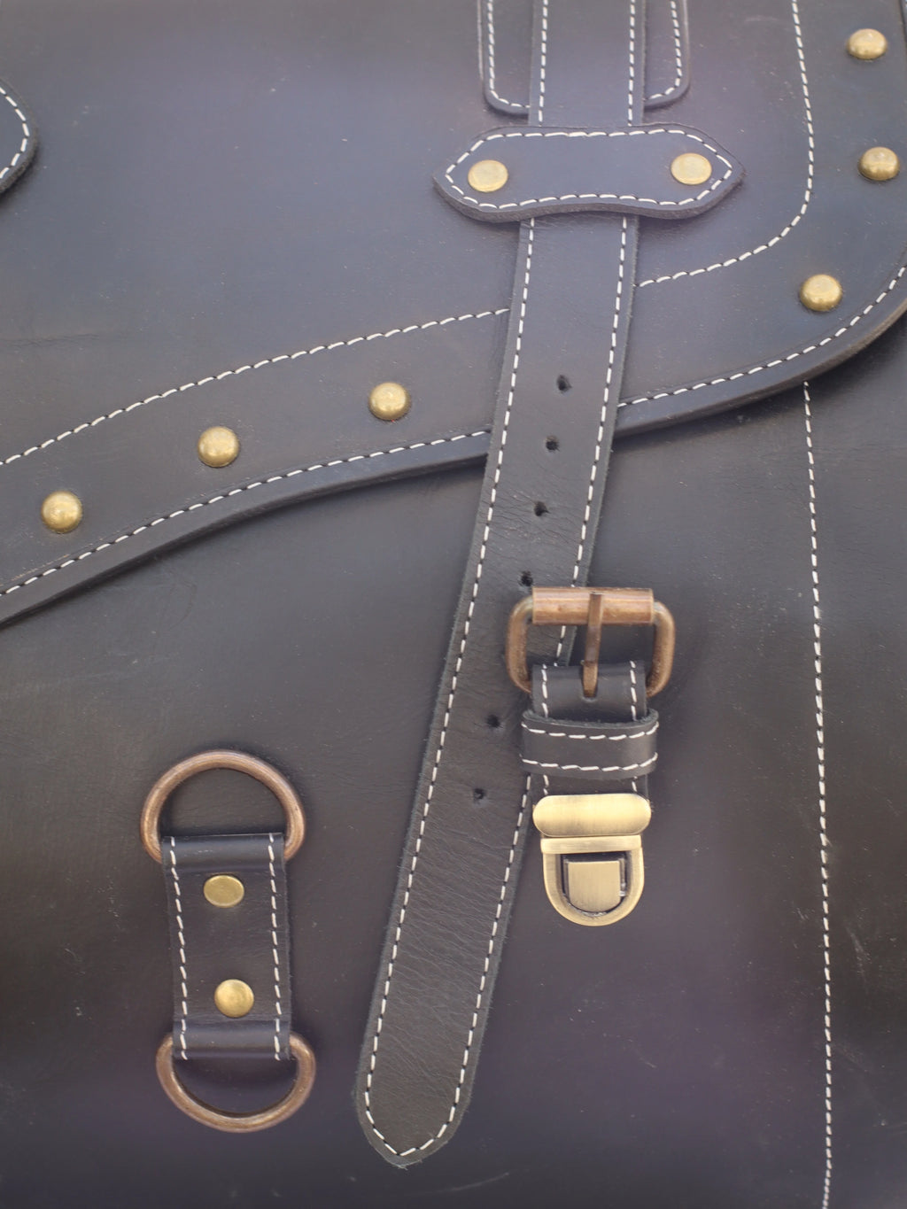 Black leather trunk luggage featuring vintage brass studs, contrast stitching, and metal buckle closures.