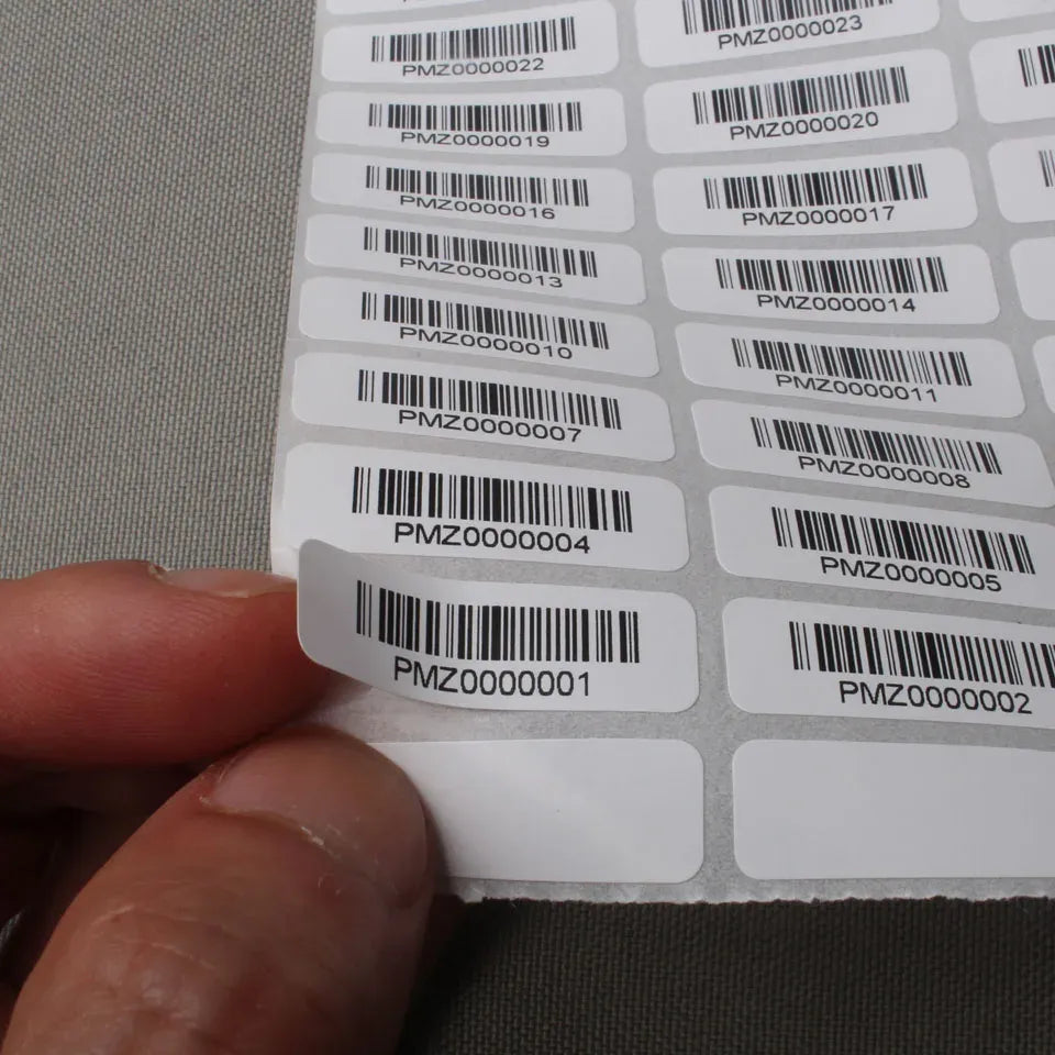 Hand lifting a corner of a barcode label sheet with white adhesive labels