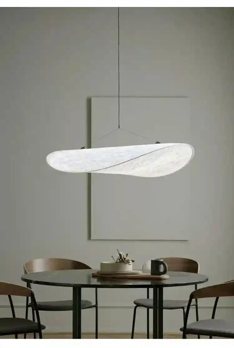 Large, wavy, white textured paper pendant light suspended by thin cables above a dining table.