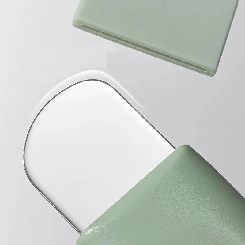 A sage green pore cleansing tool with a rounded, thin metal blade for removing blackheads.