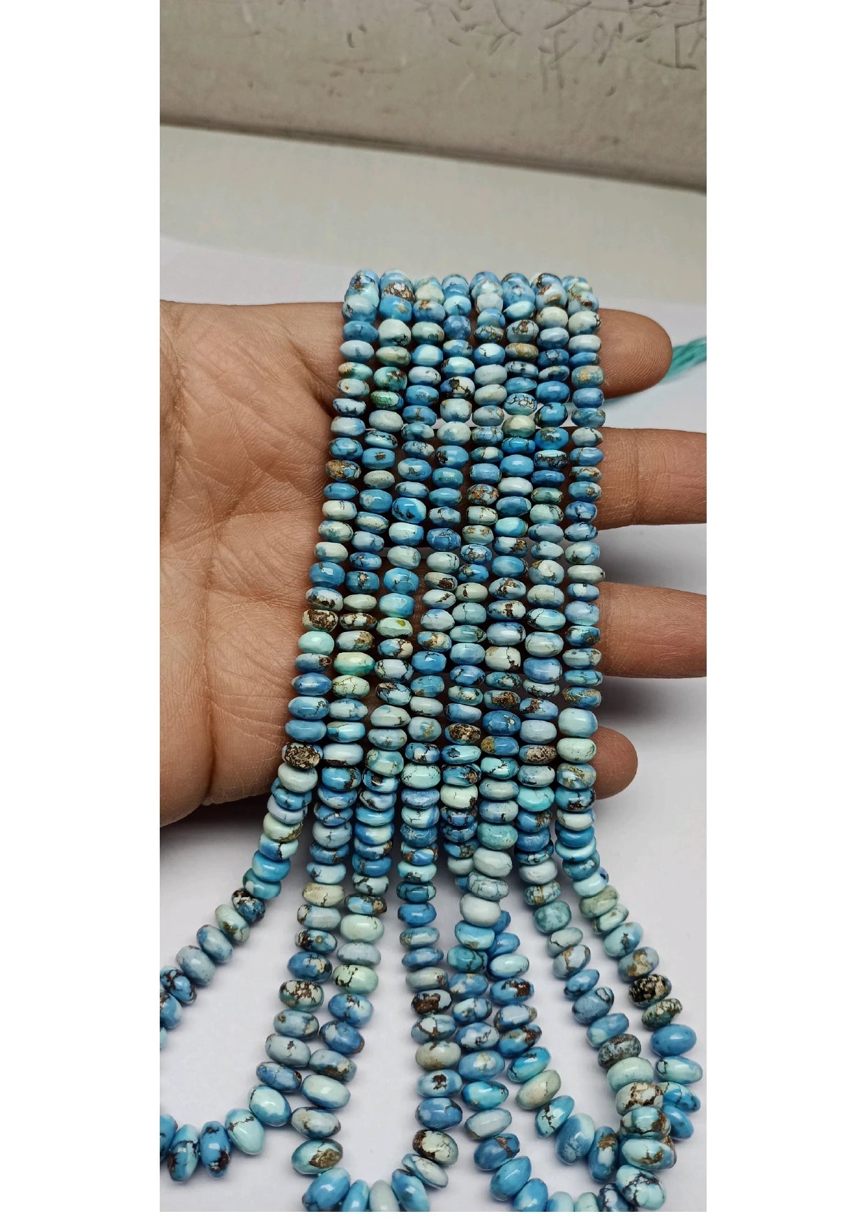 Turquoise rondelle bead strand held in hand, smooth small beads with teal and blue tones