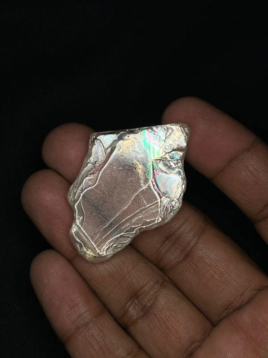 Hand holding iridescent rough gemstone, silver-toned piece with rainbow iridescence