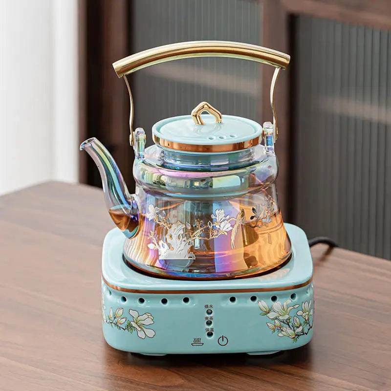 Iridescent glass electric tea kettle with floral print on a matching ceramic base heater for brewing loose leaf tea.
