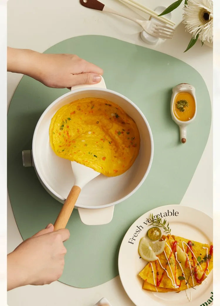 Electric skillet-style pot on a stovetop surface with lid and serving spoon.