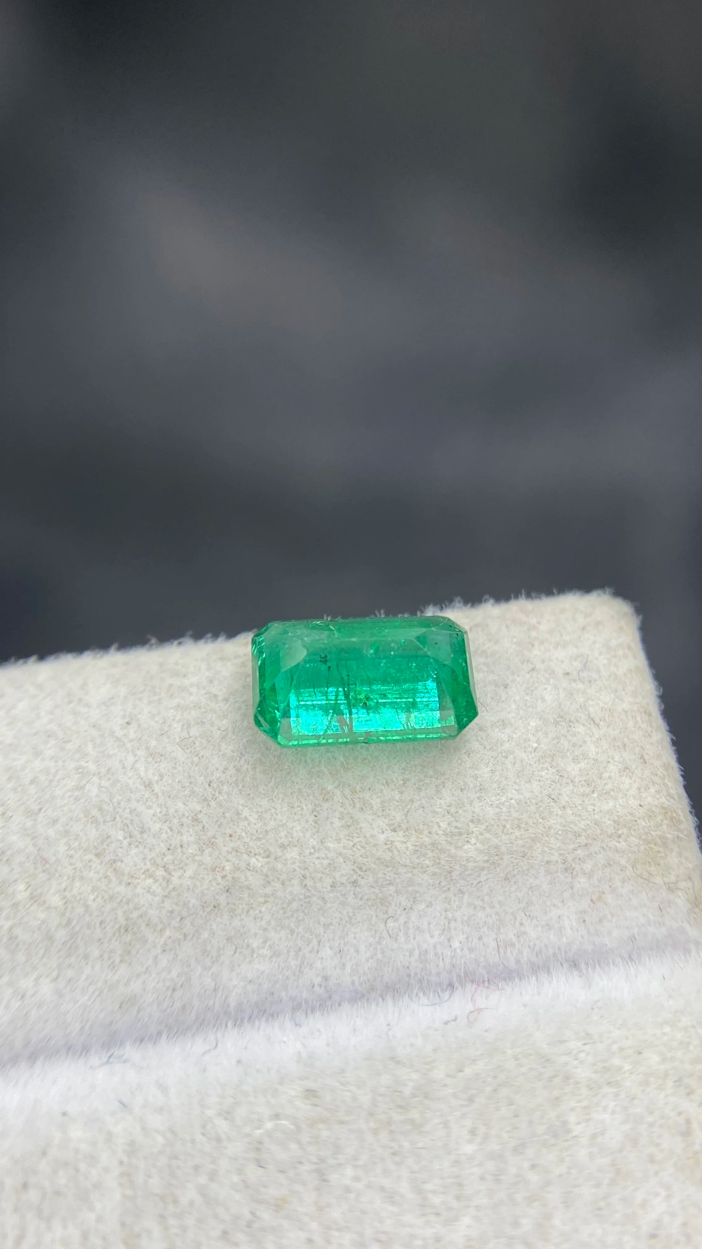 Green emerald-cut gemstone with clear facets, loose stone on white padding