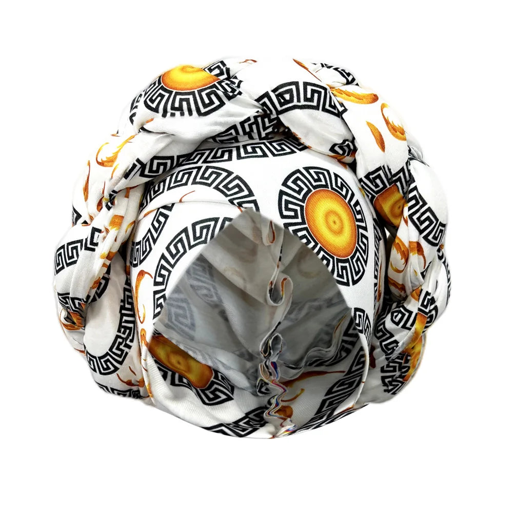 Tidesmit white fabric turban bonnet with a black Greek key and gold circular sun print, featuring a braided crown.