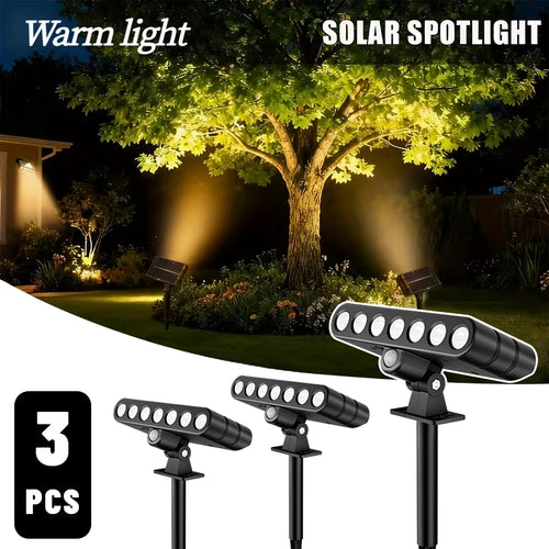 Black solar-powered LED ground spotlights with seven light heads and adjustable stakes, illuminating a tree.