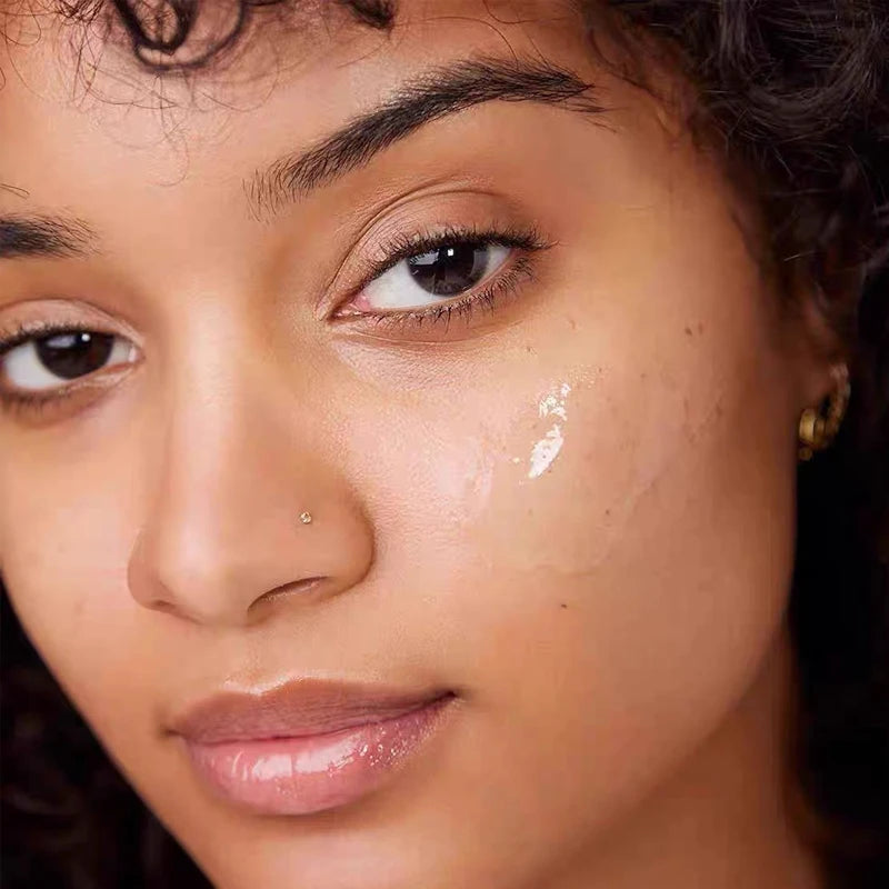 Clear, glossy e.l.f. lip balm texture applied to cheek, creating a moisturizing, high-shine finish on skin.
