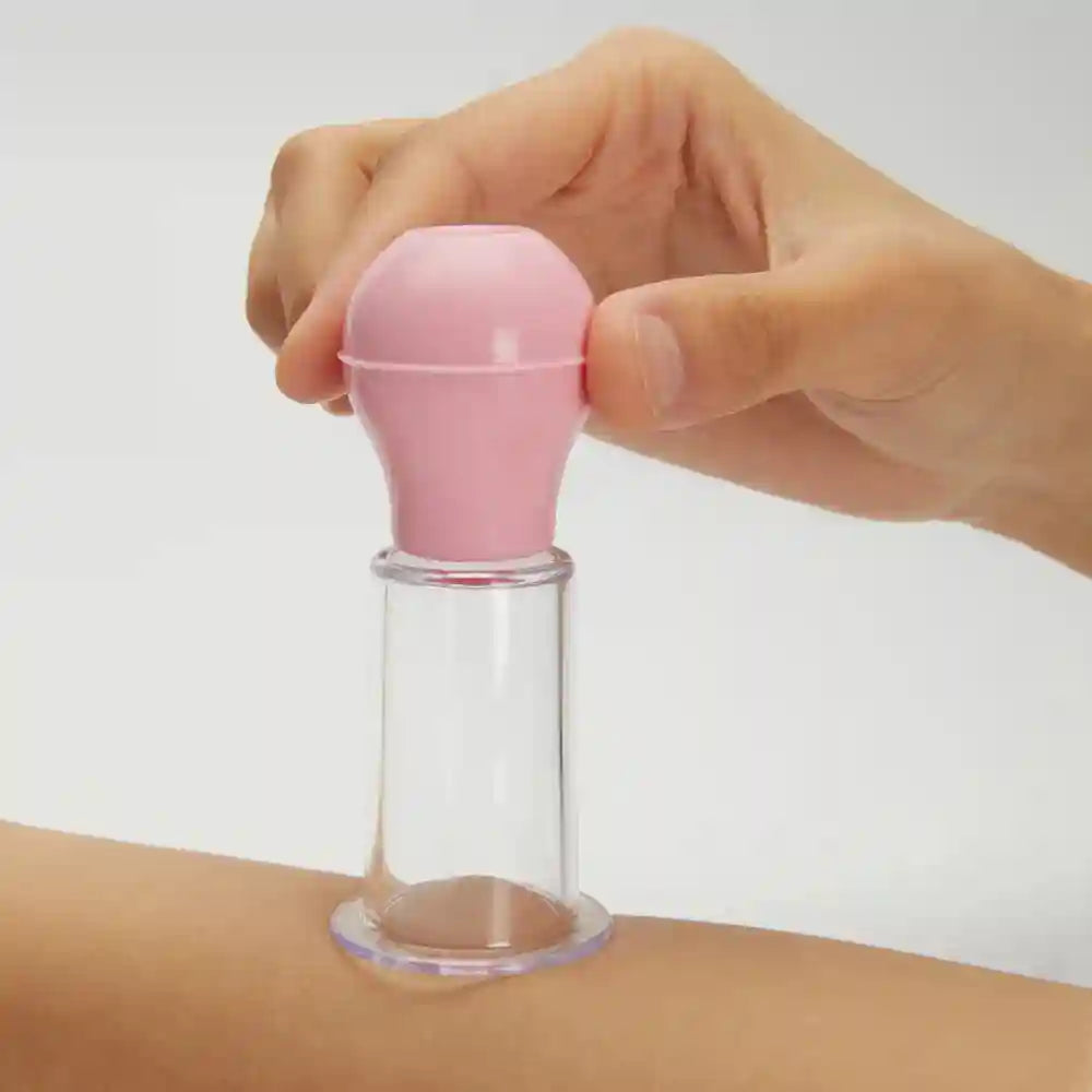 Hand holding a pink and clear vacuum cupping massager for facial skin lifting and anti-cellulite therapy.