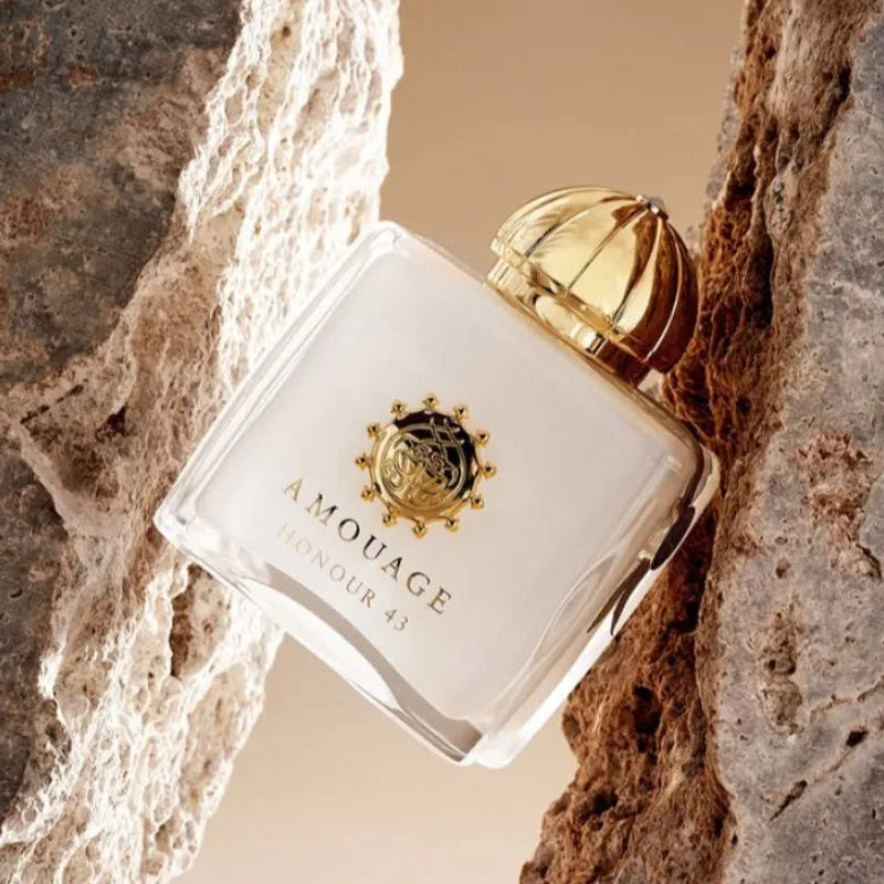 Amouage Honour 43 perfume in a square white glass bottle with a gold cap, nestled between two textured rock formations.