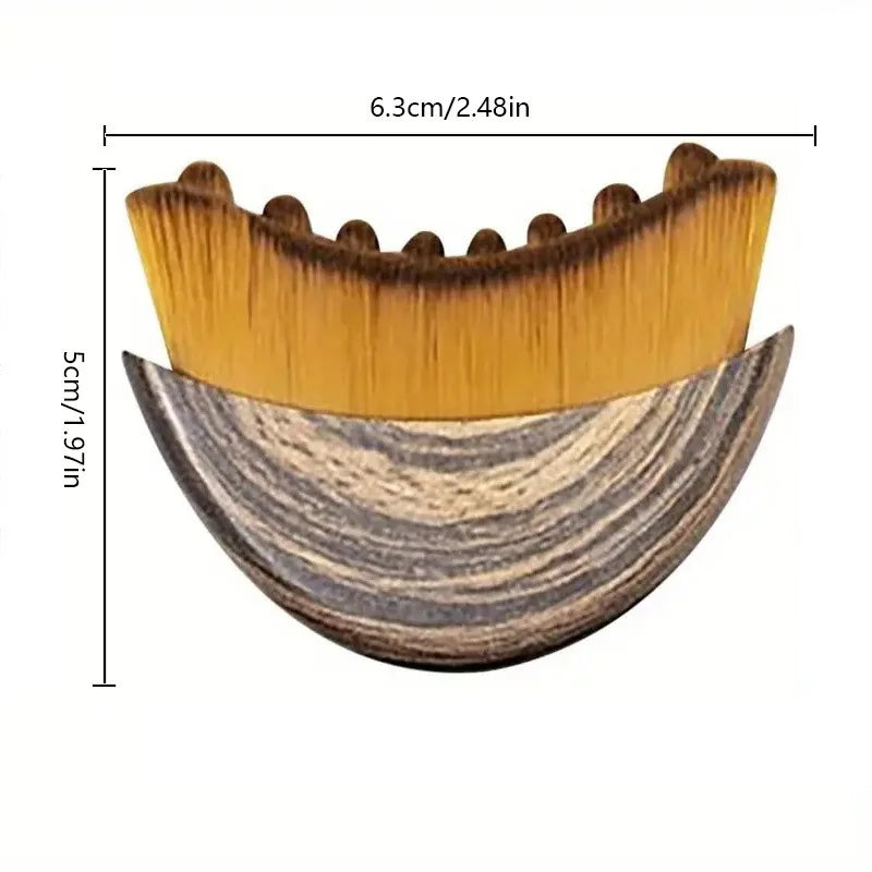 Crescent-shaped facial massage brush with a wooden handle and dense, golden-brown bristles, measuring 6.3cm by 5cm.