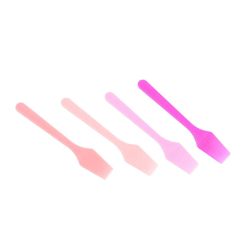 Four small plastic cosmetic spatulas in a gradient of pink shades, from soft peach to bright magenta.