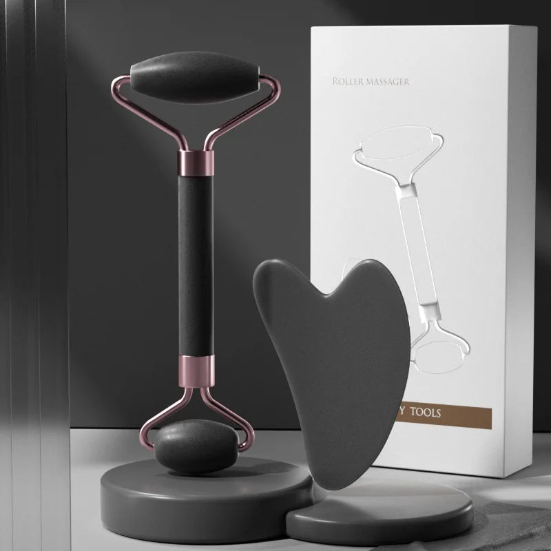 A matte black face roller with rose gold accents and a matching heart-shaped gua sha tool beside their product box.