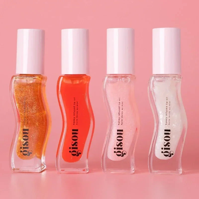 Four Gisou Honey Infused Lip Oils in colorful, high-shine, plumping gloss formulas on a pink background.
