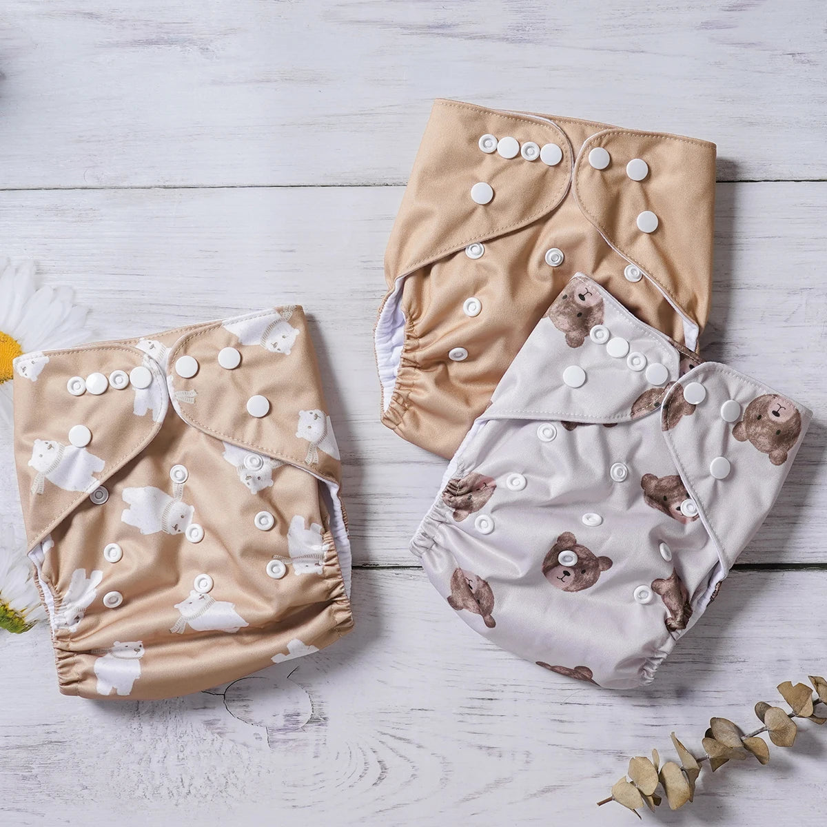 Three reusable cloth baby diapers featuring tan and bear print designs with adjustable snap closures.
