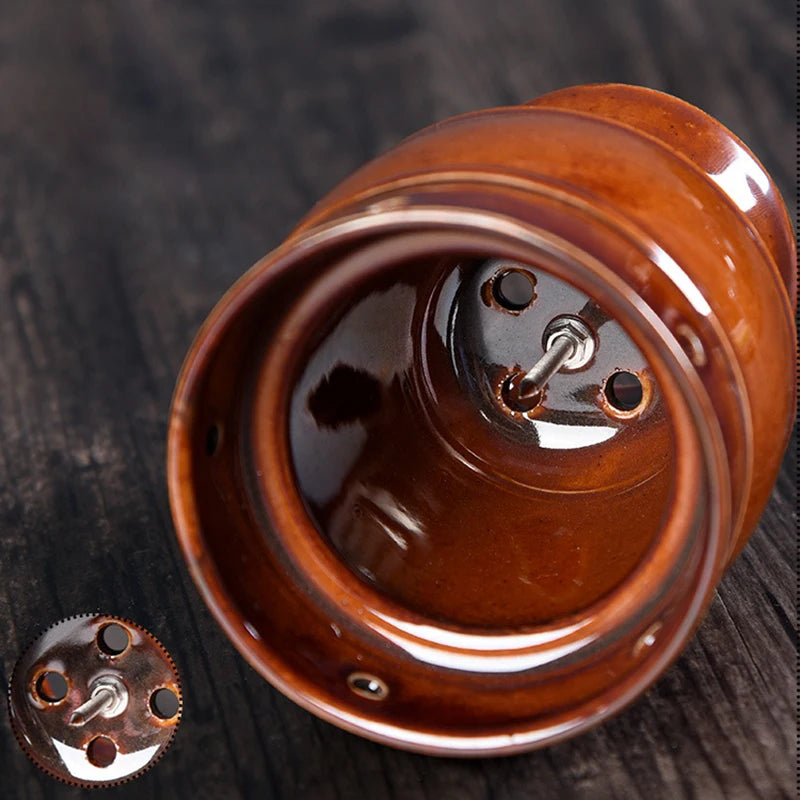 Brown ceramic moxibustion cup with a metal spike base for holding moxa sticks, shown on a dark wooden surface.
