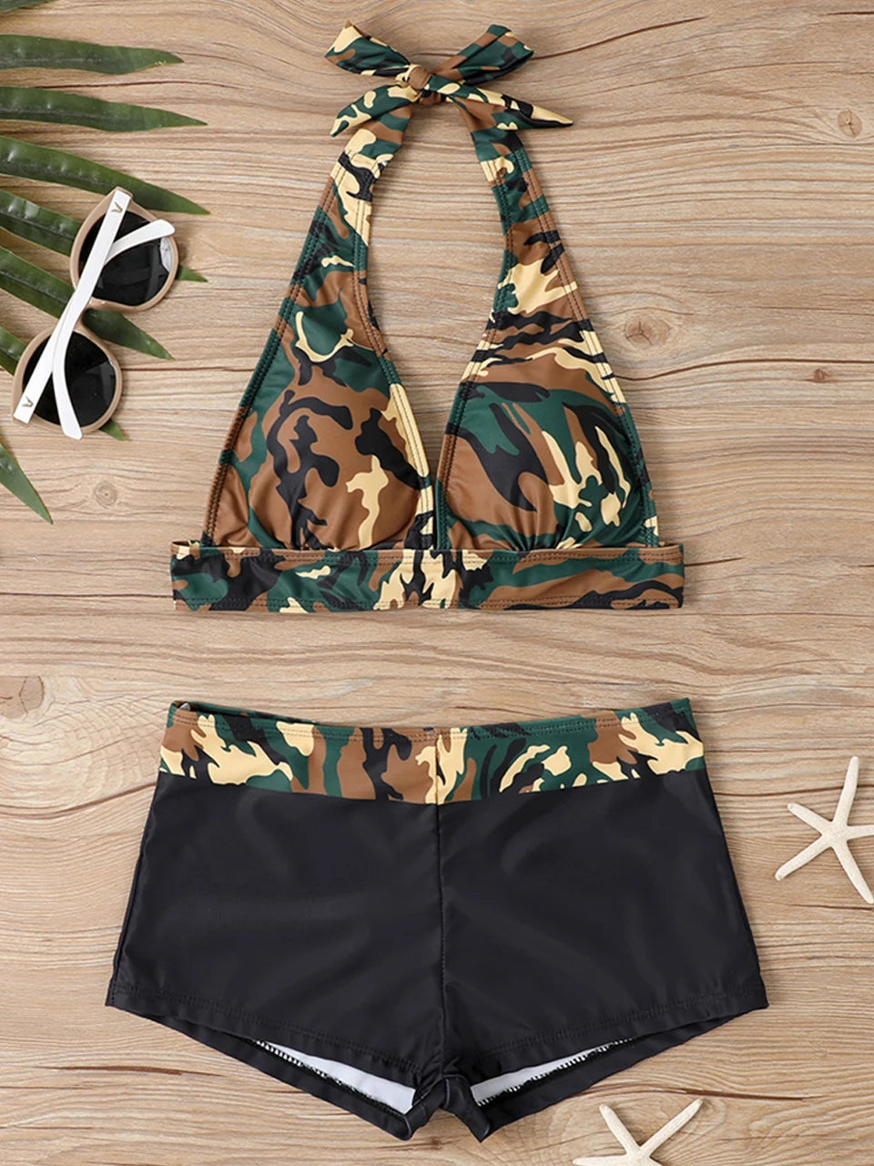 Tidesmit camouflage halter bikini top with a bow and black high-waisted shorts on a wooden surface with sunglasses.