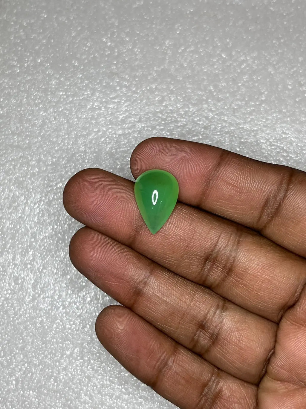 Green chrysoprase pear-shaped cabochon gemstone held in fingers, polished teardrop.