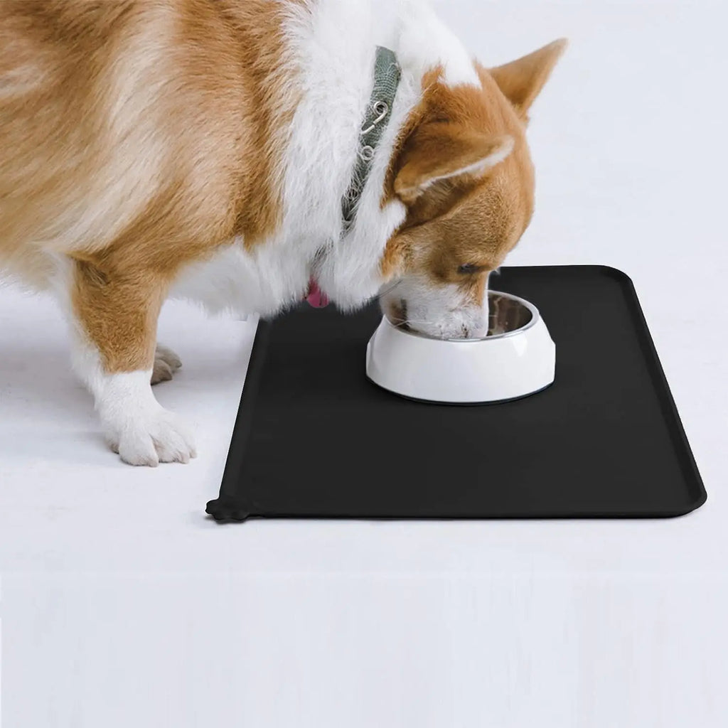 Dog eating from a bowl on a black, waterproof, BPA-free silicone pet feeding mat with raised edges to prevent spills.