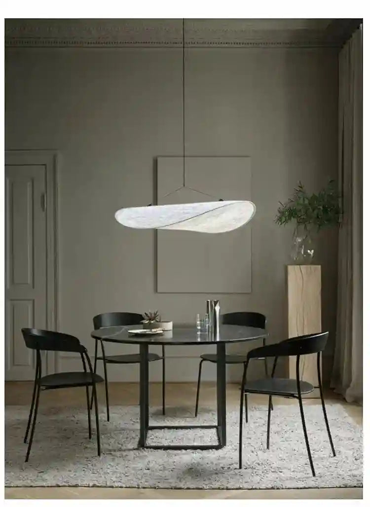 Large, wavy-edged white pendant light suspended over a round black dining table in a minimalist room.