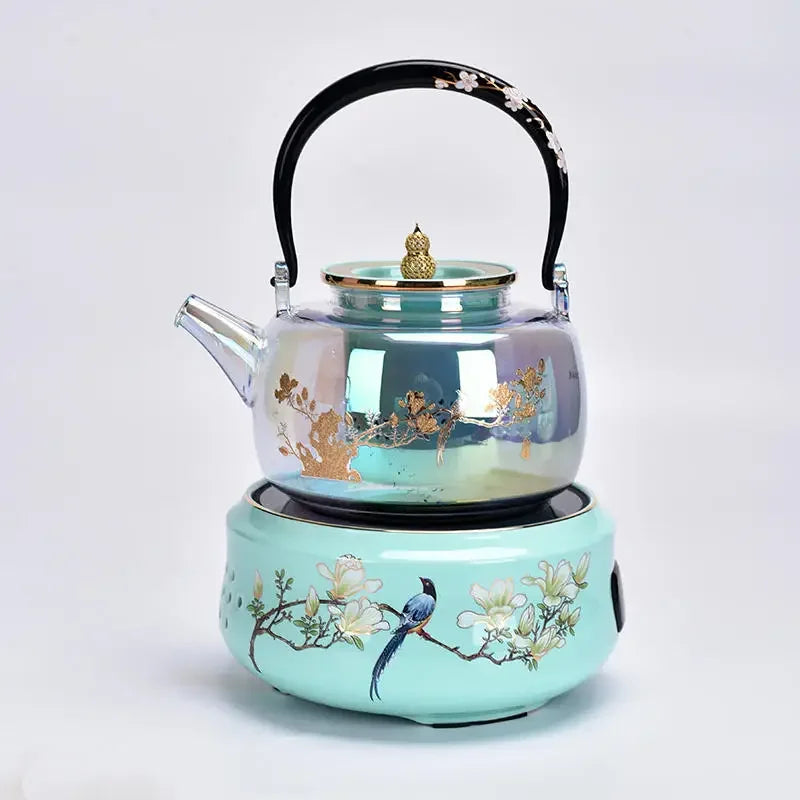 Iridescent glass tea kettle with floral design on a mint green ceramic electric stove base with bird art.