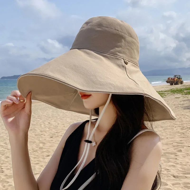 Tidesmit khaki wide-brim fabric sun hat with a chin strap, worn by a woman on a sandy beach.