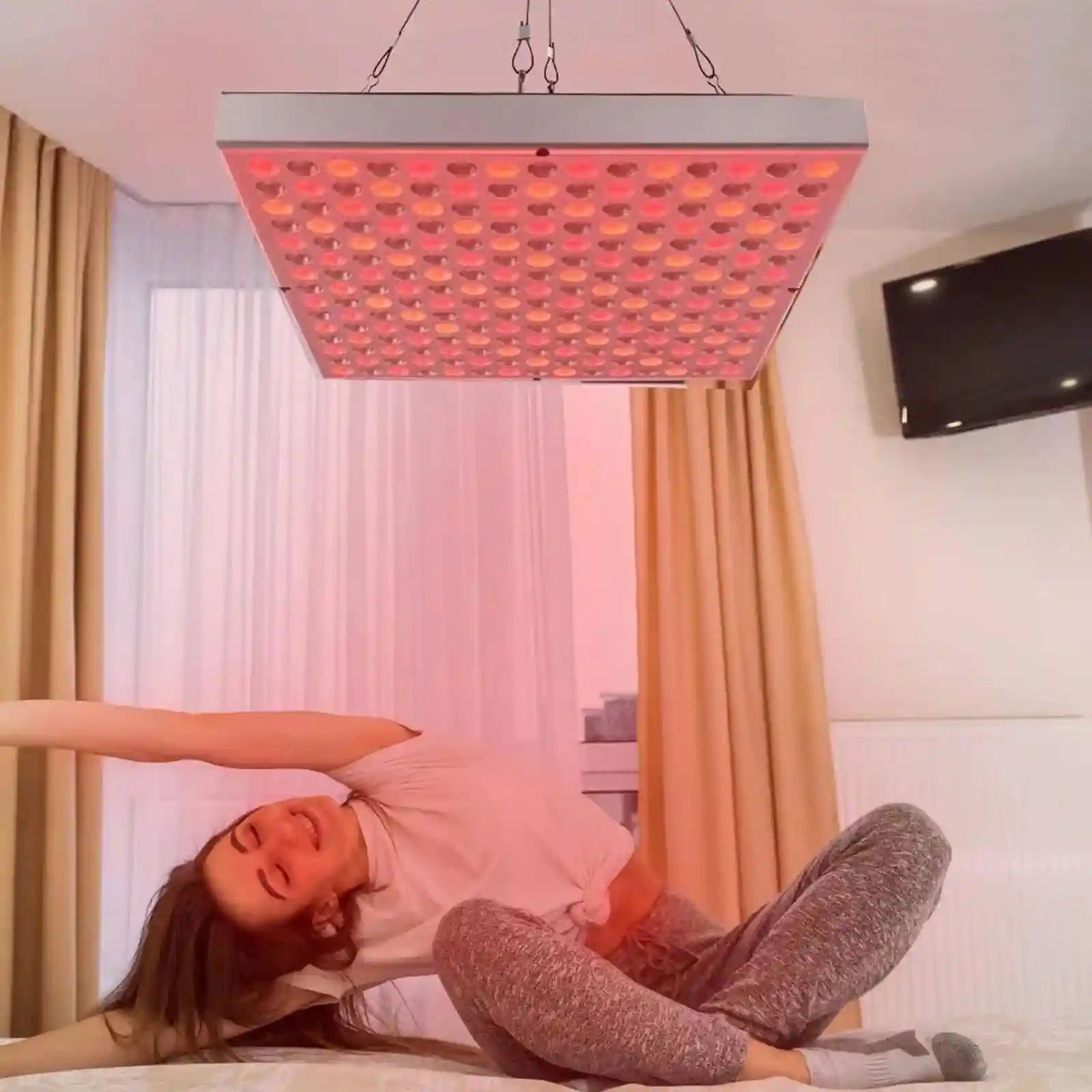 Woman doing yoga under a 45W 660nm/850nm red light therapy panel for home beauty and physiotherapy.