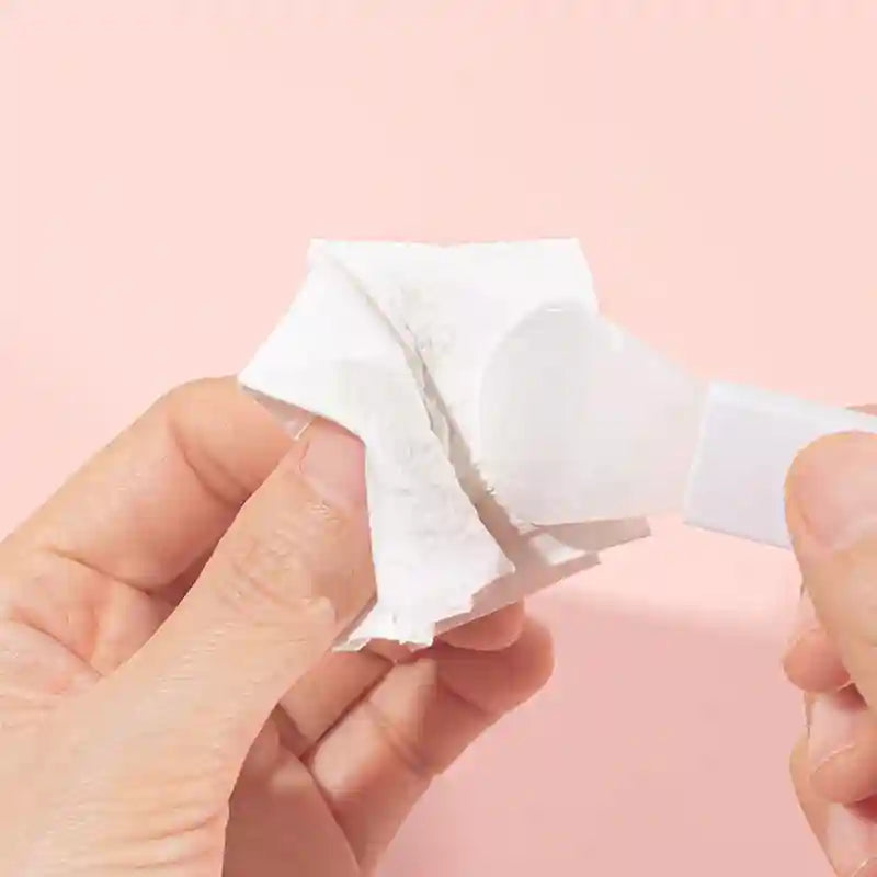 White plastic spatula applying cream onto a small, folded square of white paper for skincare or cosmetic application.