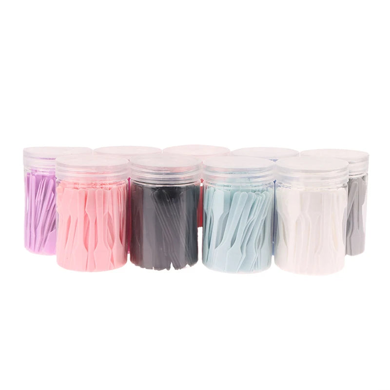 Several clear jars filled with small, colorful plastic cosmetic spatulas for mixing creams and makeup.