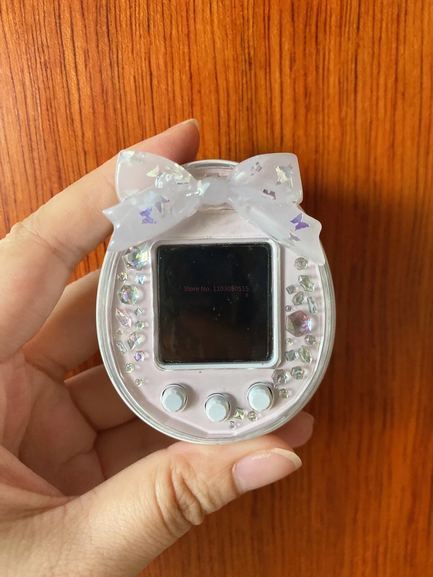 Pink Tamagotchi Uni hard shell case with crystal gems and butterfly bow for stylish electronic pet protection.